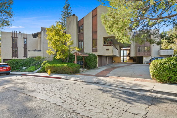 Front view of a multi-story building with a sloped driveway and covered parking.