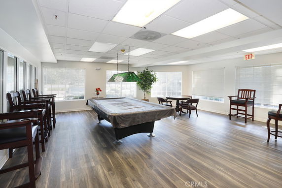 Room with a pool table and chairs, featuring large windows and wooden flooring.