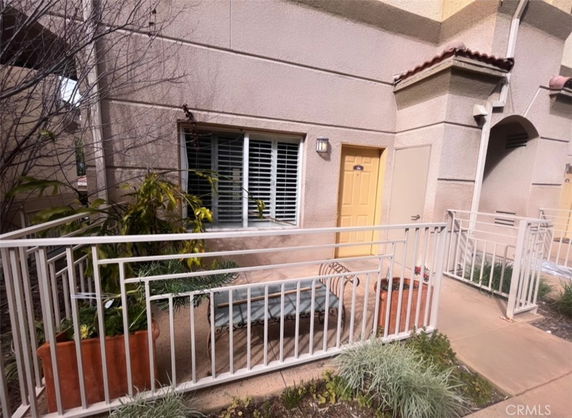 Front view of a building with beige stucco walls, a yellow door, and a railing-enclosed patio area.