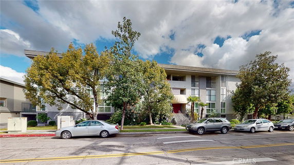 Front view of a multi-story residential building with trees and parked cars.