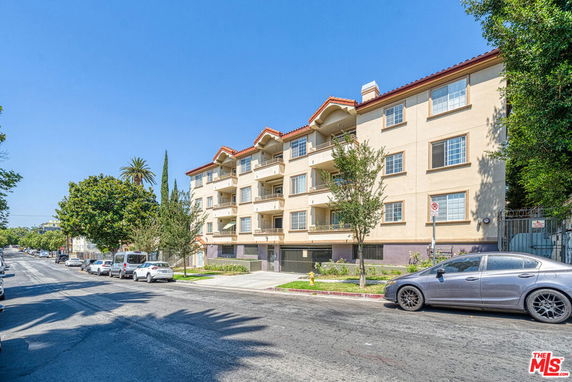 Front view of a multi-story apartment building with balconies and a red-tiled roof.