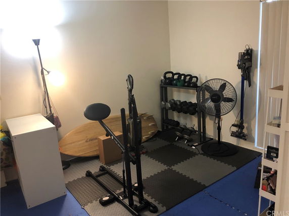 Indoor home gym area with exercise equipment including weights, exercise machine, and a fan.