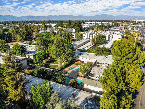 Aerial view of residential area with multiple buildings and a swimming pool surrounded by trees.