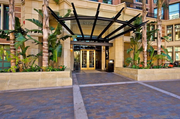 Front view of a building entrance with a glass canopy and surrounding plants.
