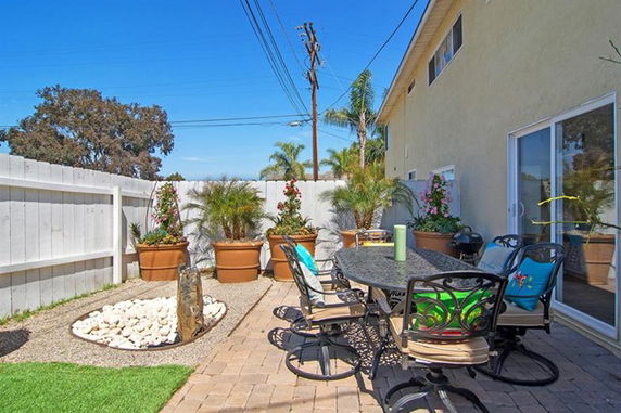 Outdoor patio area with table and chairs, potted plants, and decorative stones.