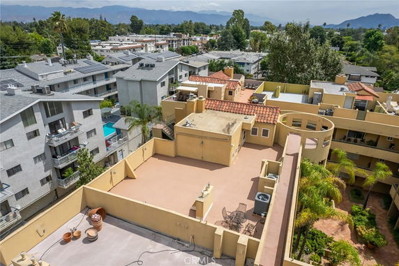 Rooftop view featuring patios and seating, with surrounding buildings and greenery in the background.