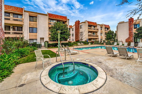 Outdoor view of a residential complex featuring a swimming pool and hot tub with surrounding lounge chairs.