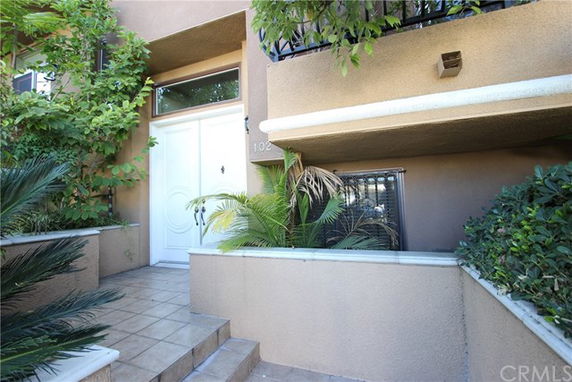 Front view of a multi-story building with a white entrance door and surrounding greenery.