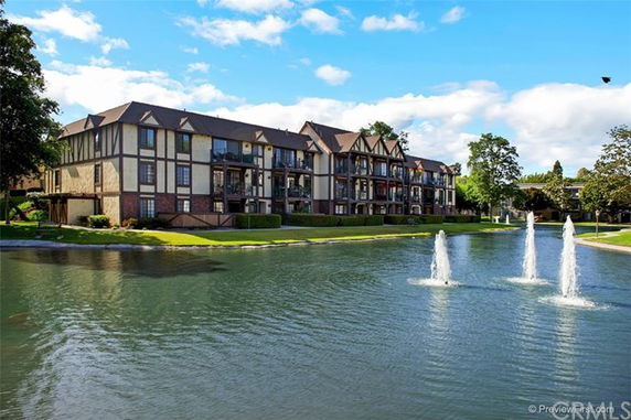 Front view of a multi-story residential building with Tudor-style architecture adjacent to a pond with fountains.