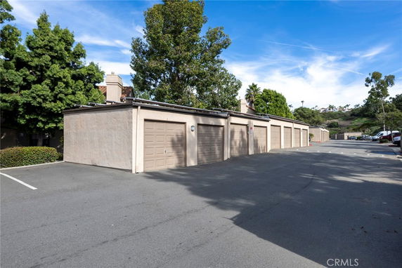 Outdoor parking area with multiple garage doors and surrounding trees.
