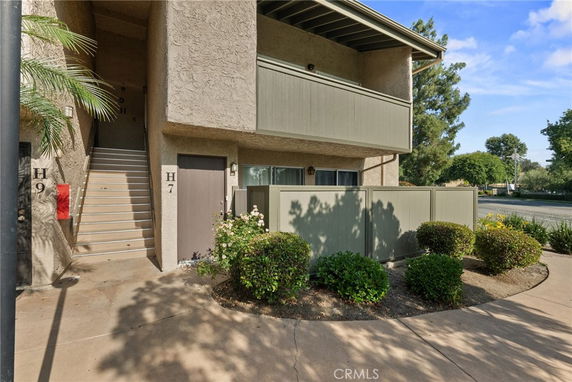 Front view of a two-story residential building with a staircase and fenced patio.