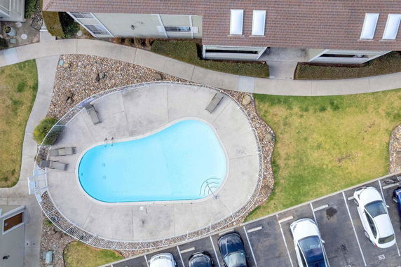 Aerial view of a swimming pool next to a building and parking area.