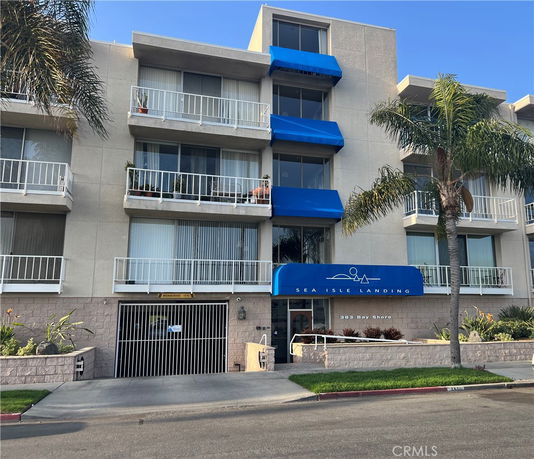 Front view of a multi-story building with balconies and blue awnings.