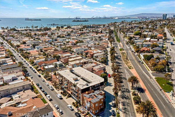 Aerial panoramic view of a coastal residential area with numerous houses and roads, overlooking the ocean and distant port facilities.