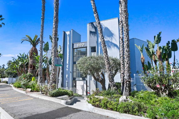 Front view of a modern multi-story building with a glass entryway and surrounding palm trees.