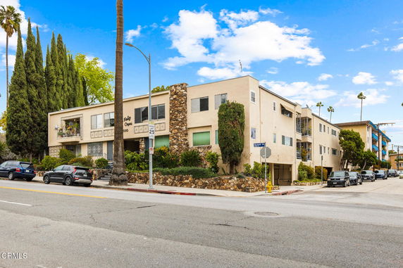 Front view of a multi-story apartment building with a stone exterior on the corner of a street.