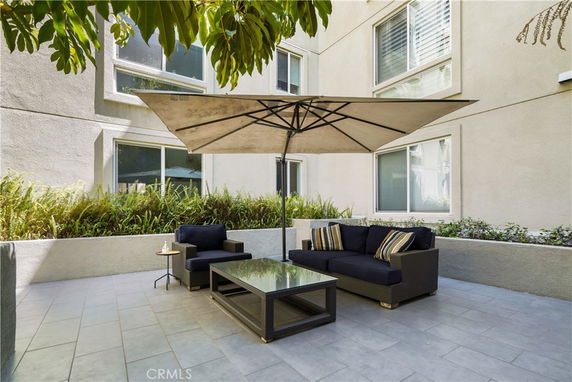 Outdoor patio area with a large umbrella, sofa, and coffee table in front of a building.