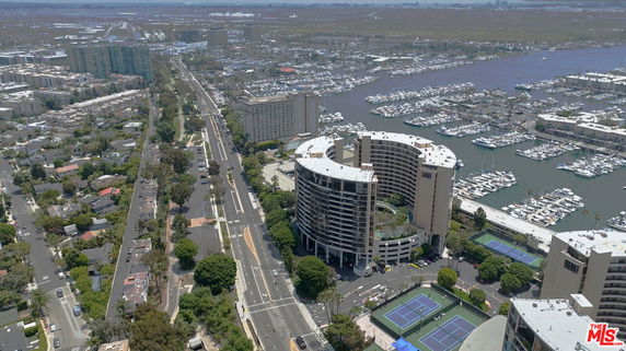 Panoramic view of a cityscape with a curved building, tennis courts, and a marina.