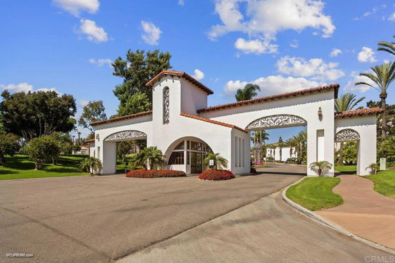 Front view of an entrance structure with arches and a tower, surrounded by greenery.