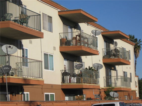 Front view of a multi-story apartment building with balconies and satellite dishes.