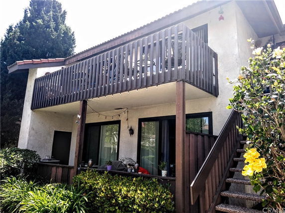 Front view of a two-story house with a wooden balcony and exterior staircase.