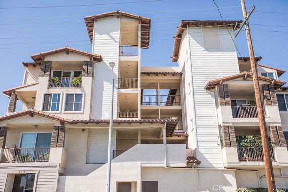 Front view of a multi-story residential building with balconies and tiled roof.