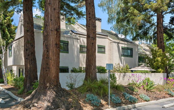 Front view of a multi-story building with a modern design and slanted roofs, surrounded by tall trees.