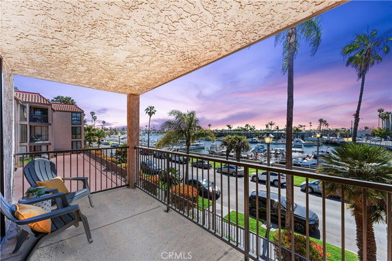 Balcony view overlooking a marina with boats and palm trees at sunset.