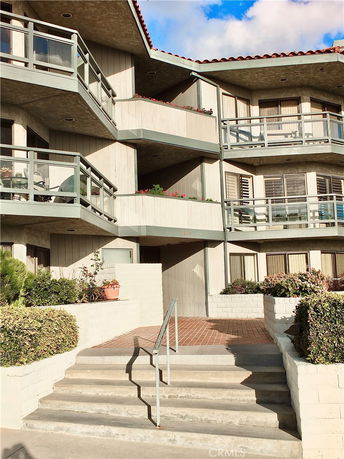 Front view of a multi-story building with balconies and stairs leading to the entrance.
