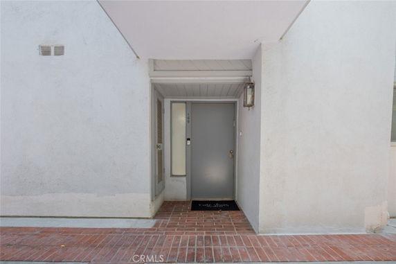 Front view of a building entrance with a gray door and red brick flooring.