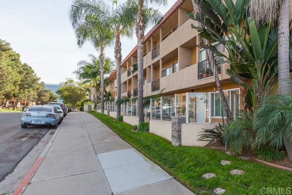 Front view of a multi-story building with balconies and surrounded by palm trees.