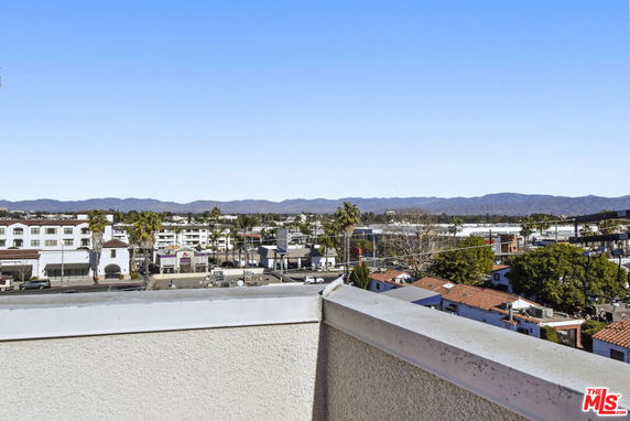 Panoramic view of a cityscape from a rooftop, with buildings and a mountain range in the distance.