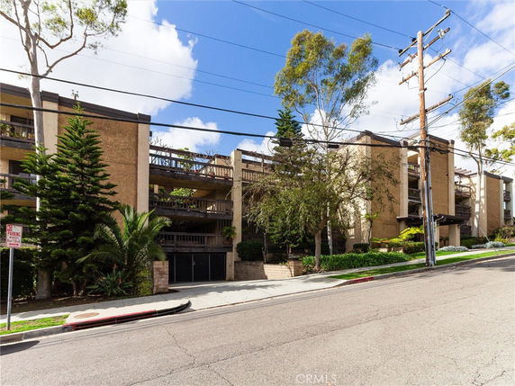Front view of a multi-story residential building with balconies and surrounded by trees.
