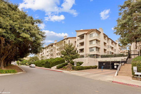 Front view of a multi-story apartment building with balconies and a gated parking entrance.