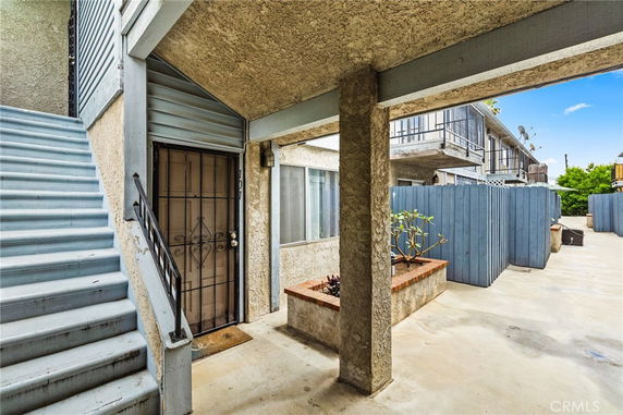 Exterior view of an apartment entrance with stairs and a blue fence.