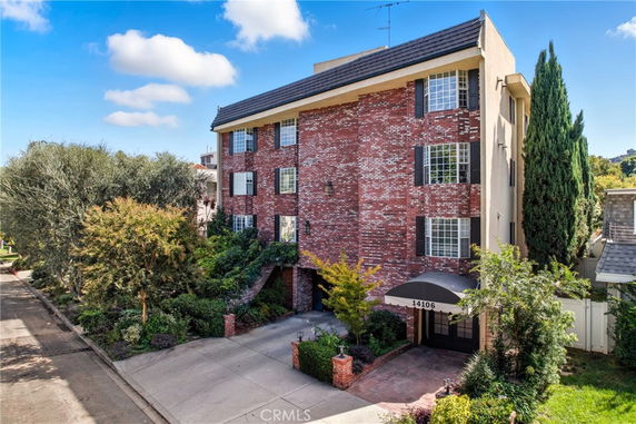 Front view of a multi-story brick building with an arched entrance and shutters on windows.