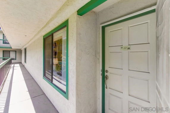 Exterior corridor view of an apartment door marked 207, with green trim surrounding door and windows.