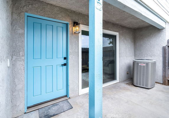 Entrance view of a house with a blue front door and adjacent sliding glass door, featuring an exterior air conditioning unit.