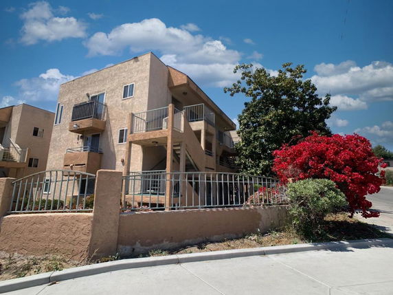 Front view of a multi-story building with balconies and surrounding fence.