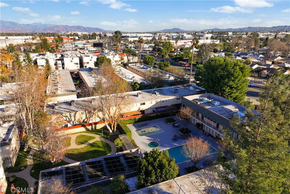 Panoramic view of a residential area with multiple buildings, surrounding greenery, and mountains in the distance.