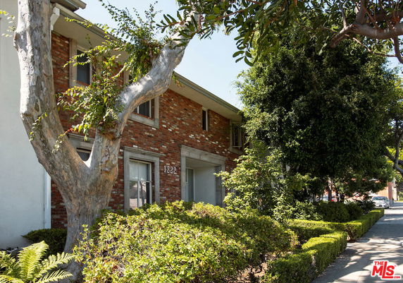 Front view of a two-story brick house with greenery and trees surrounding it.