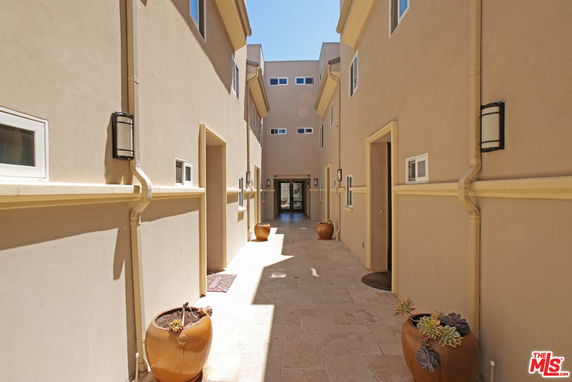 Narrow outdoor corridor between buildings with beige walls and potted plants.