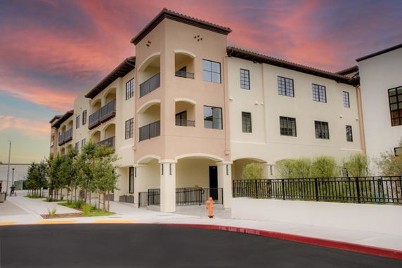 Front view of a three-story building with balconies and a paved walkway.