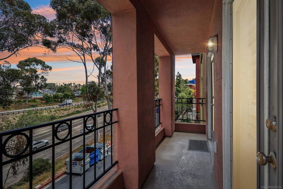View from a balcony looking out towards a tree-lined street and distant buildings at sunset.