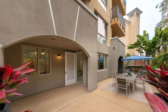 Outdoor patio area with table, chairs, and umbrella adjacent to a multi-story building.