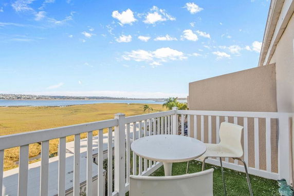 A balcony with a table and two chairs overlooking a wide expanse with water and landscape in the distance.