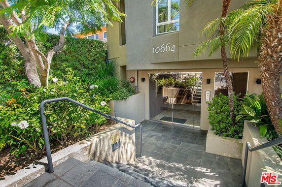Front view of a building entrance with glass doors and surrounding foliage.