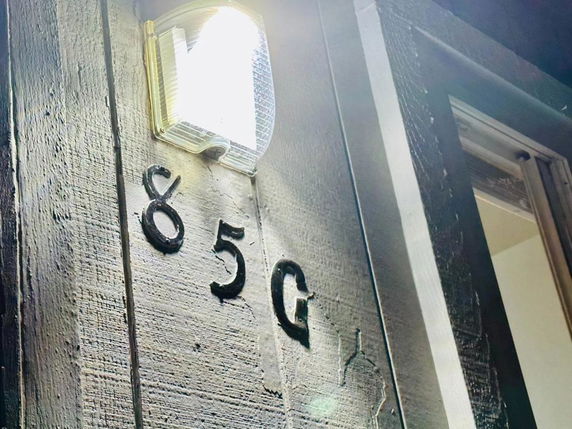 Close-up view of a building's exterior wall with the number 85G and a wall light.