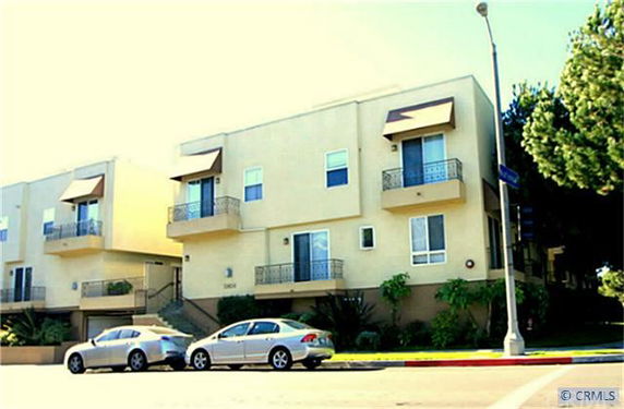 Front view of a modern multi-story building with balconies and several cars parked in front.