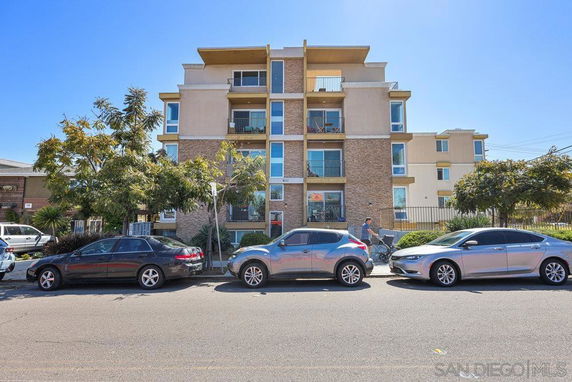 Front view of a multi-story apartment building with balconies and parked cars in front.